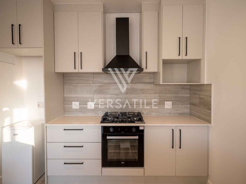 Modern kitchen featuring sleek white cabinetry, stone countertops, a gas hob, electric oven, and a stylish wood-look tiled backsplash.