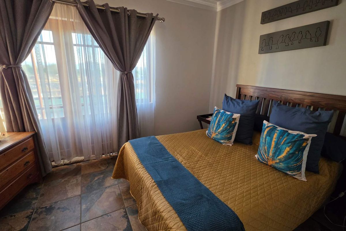 A well-maintained bedroom featuring tiled flooring, neutral wall finishes, and large windows with curtains, providing a comfortable and functional living space.