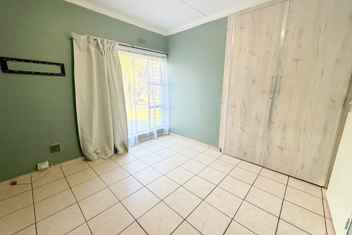 A vacant bedroom featuring tiled flooring, built-in cupboards, and a window with security bars, offering a blank canvas for personalization.