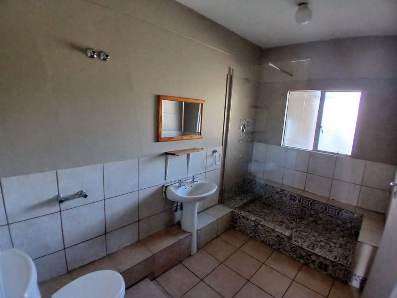 A functional bathroom featuring a pedestal basin, walk-in shower with decorative tiling, and neutral wall finishes, currently vacant and ready for updates.
