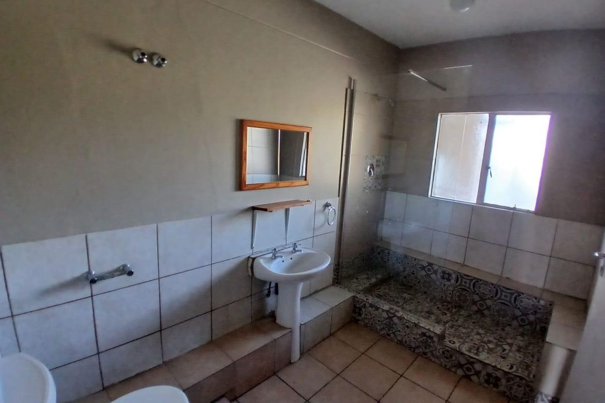 A functional bathroom featuring a pedestal basin, walk-in shower with decorative tiling, and neutral wall finishes, currently vacant and ready for updates.