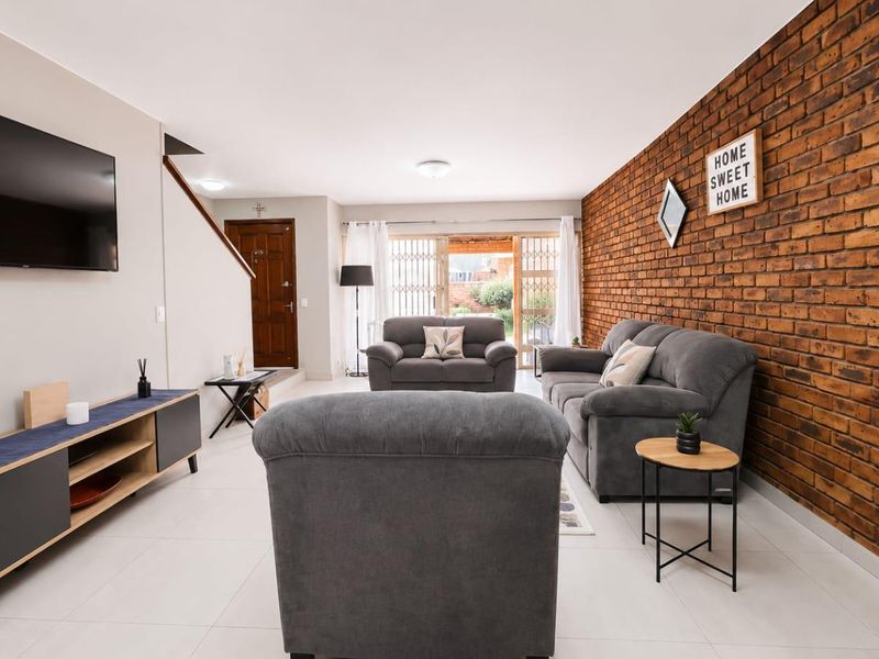 Spacious living room featuring a prominent exposed brick wall, neutral tiled flooring, and direct access to the outdoor area through a sliding glass door.