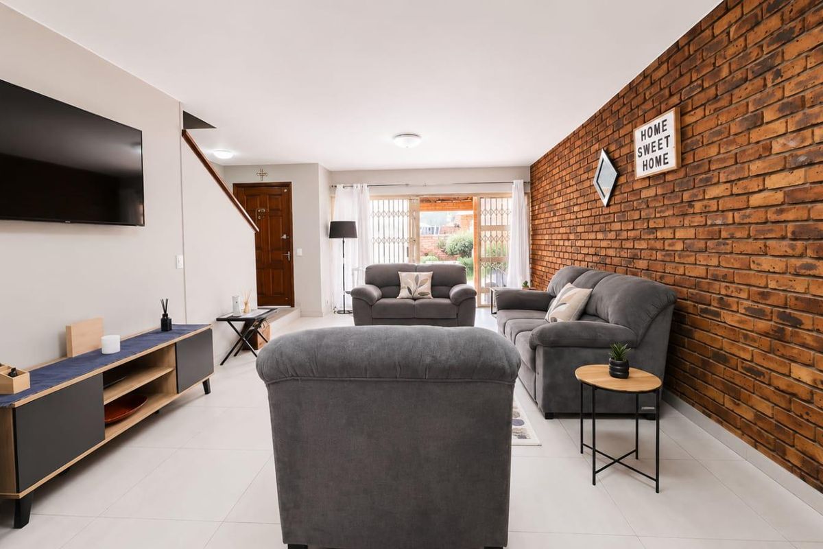 Spacious living room featuring a prominent exposed brick wall, neutral tiled flooring, and direct access to the outdoor area through a sliding glass door.
