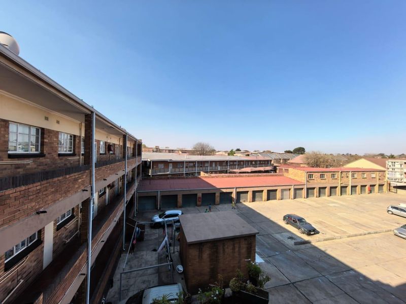 An elevated view of the apartment complex courtyard, featuring face brick building facades, paved parking area, and a row of garages.