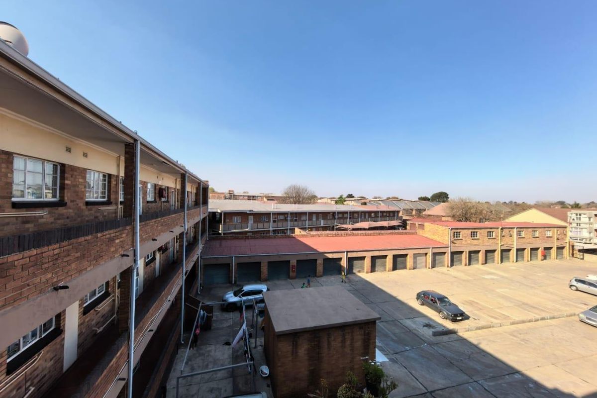 An elevated view of the apartment complex courtyard, featuring face brick building facades, paved parking area, and a row of garages.