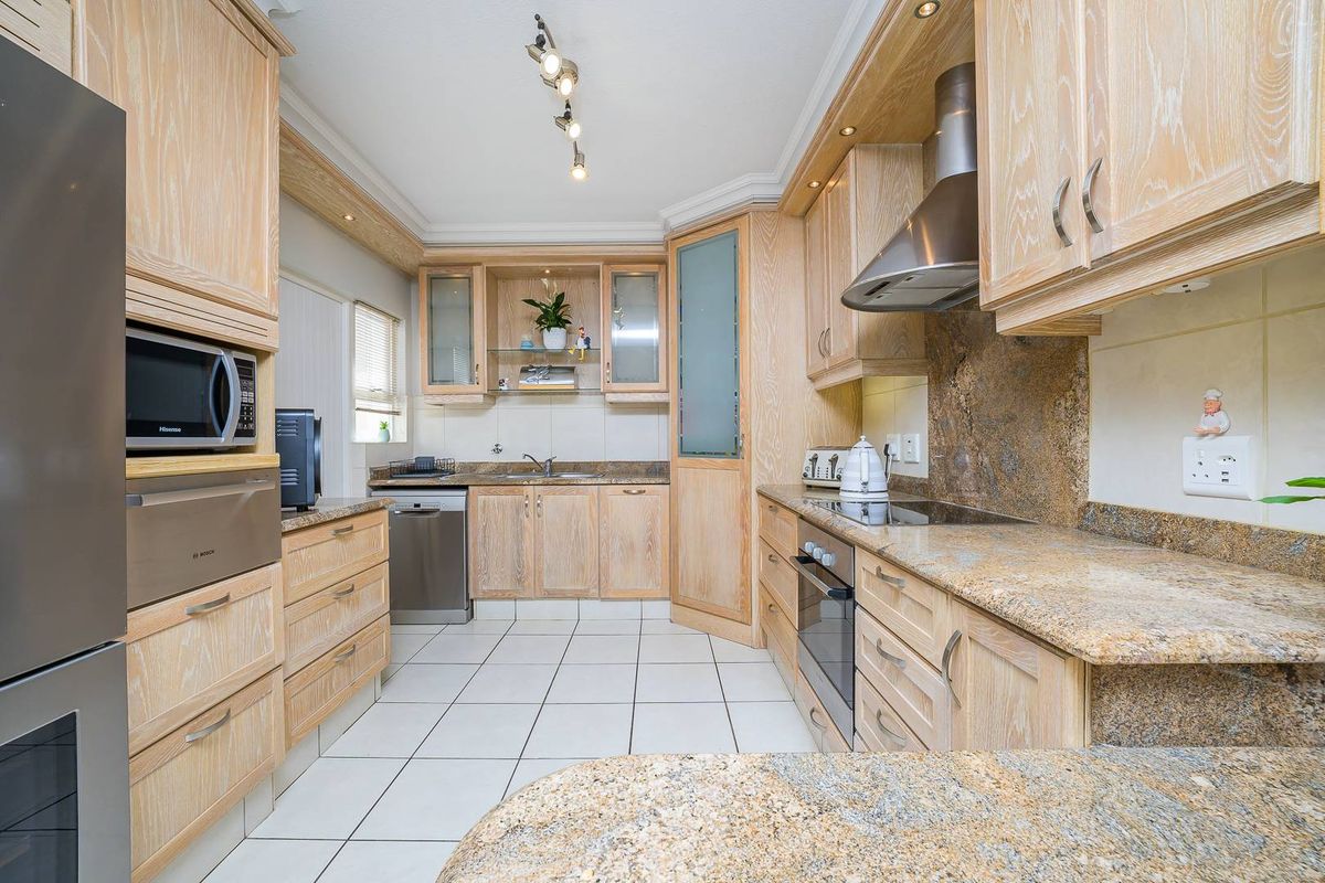 A well-maintained kitchen featuring light wood cabinetry, granite countertops, a built-in oven, hob, and stainless steel extractor fan.