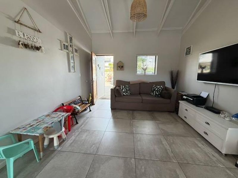 A living room featuring large format floor tiles, exposed beam ceilings, and direct access to an outdoor area.