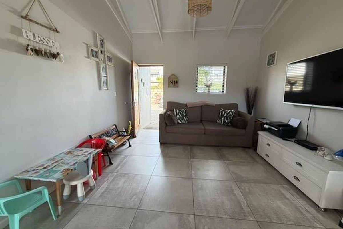 A living room featuring large format floor tiles, exposed beam ceilings, and direct access to an outdoor area.