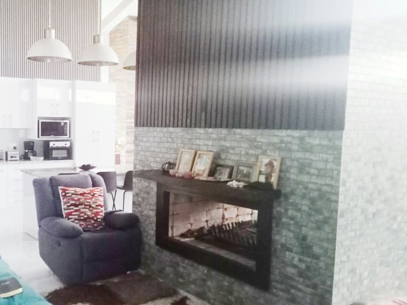 Open plan living area featuring a modern brick-clad fireplace with corrugated metal accents, adjacent to a contemporary kitchen with white cabinetry.