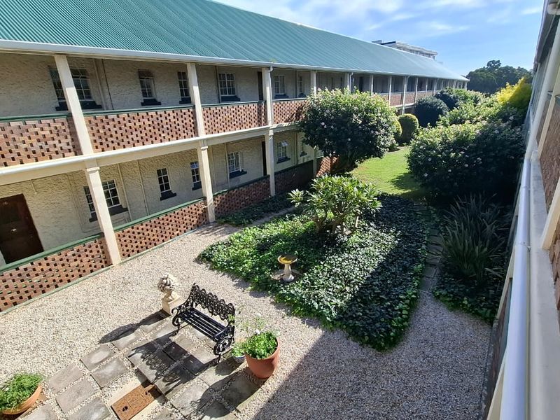 A view of the apartment complex exterior featuring a well-maintained communal garden, gravel courtyard, and brick facade with covered walkways.