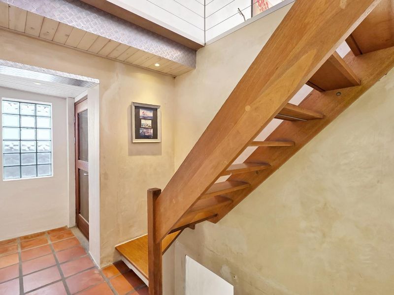 Entrance foyer featuring a wooden staircase, terracotta floor tiles, and a glass block window, providing a bright and textured transition space.