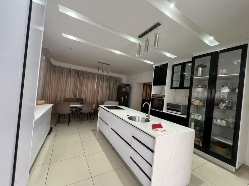 Modern open-plan kitchen featuring a central island with an undermount sink, sleek white cabinetry, built-in oven, and integrated glass-front display units.