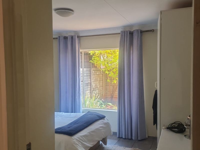 A bedroom featuring a built-in wardrobe, tiled flooring, and a window overlooking the garden area.