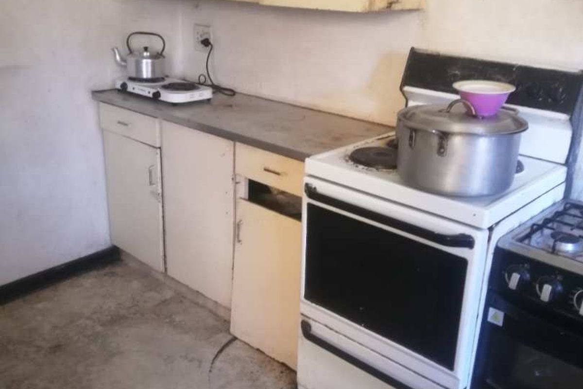 A dated kitchen area featuring basic cabinetry, a freestanding stove, and worn flooring, offering significant potential for renovation and modernization.