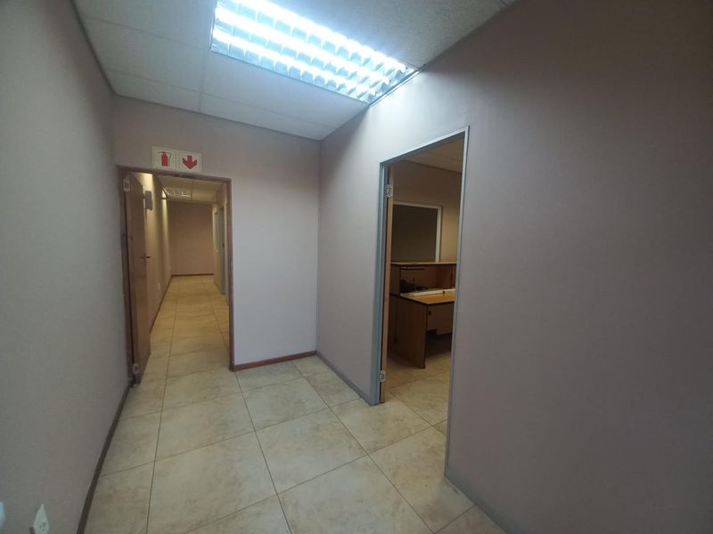 A functional office hallway with tiled flooring, suspended ceiling, and recessed lighting, providing access to adjacent office spaces.