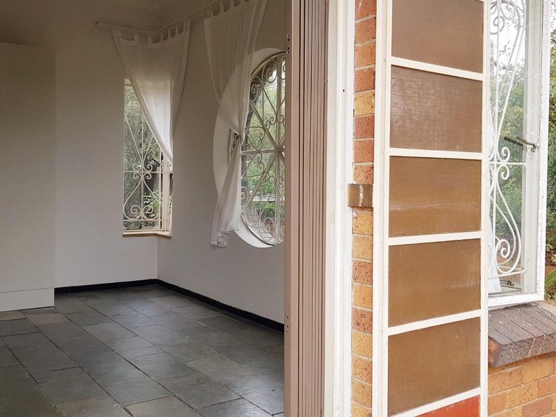 An empty living area featuring slate tile flooring, a unique circular window with security bars, and direct access to the exterior.