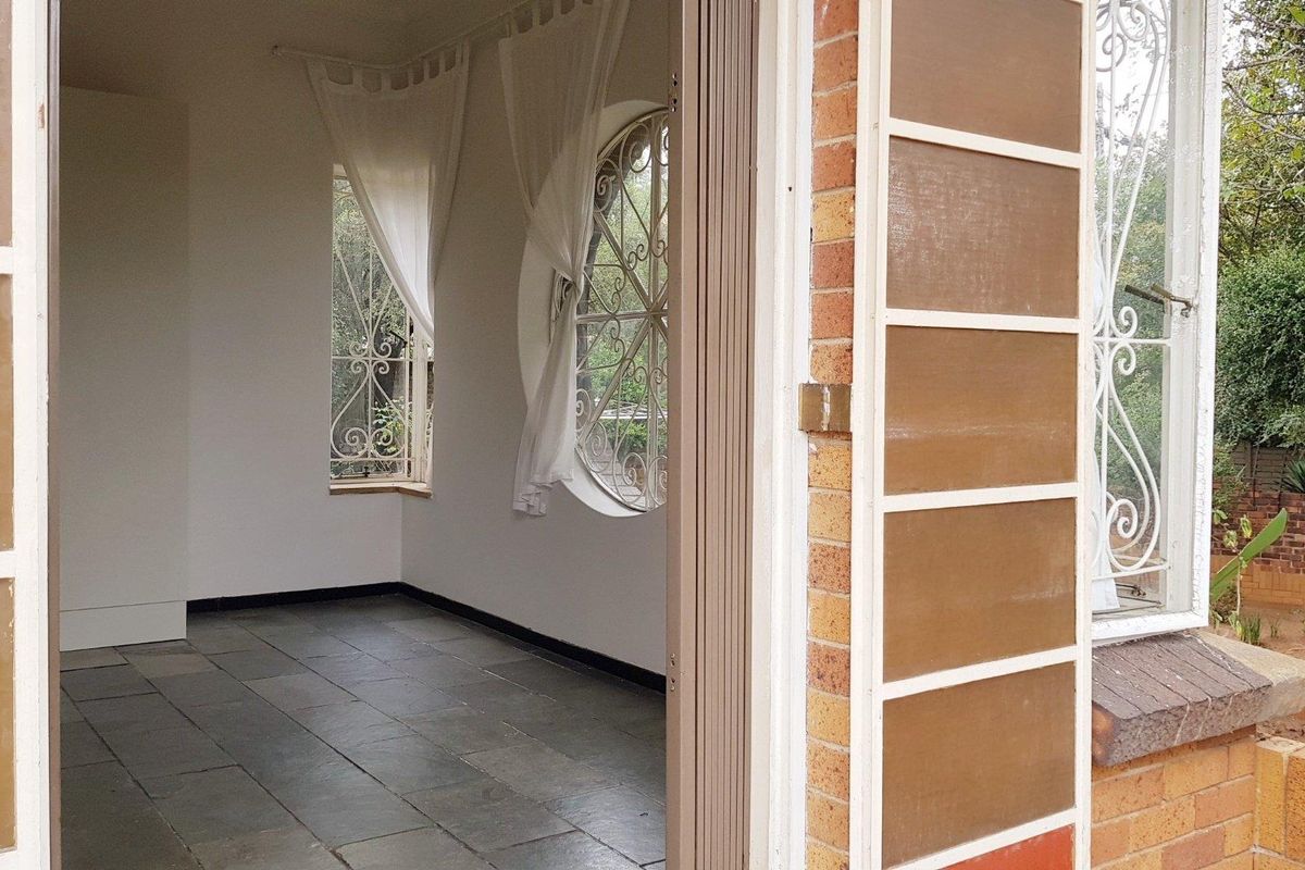 An empty living area featuring slate tile flooring, a unique circular window with security bars, and direct access to the exterior.