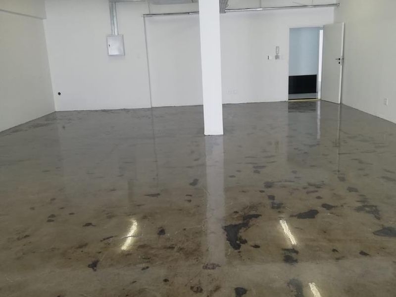 An open-plan office space featuring polished concrete floors, exposed ceiling conduit, and a central structural support column.