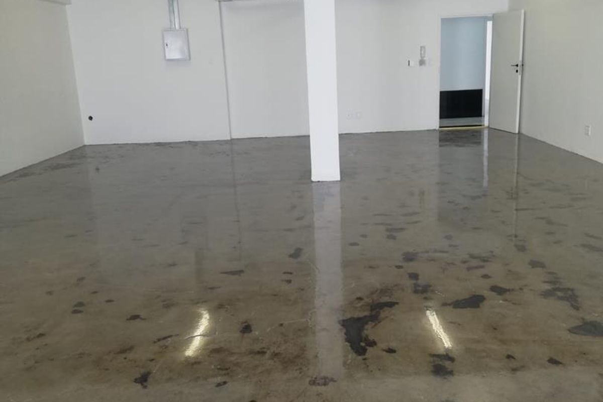 An open-plan office space featuring polished concrete floors, exposed ceiling conduit, and a central structural support column.