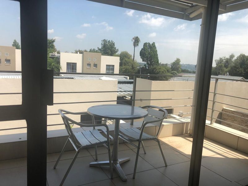 A covered balcony featuring tiled flooring and metal railings, offering an elevated view of the surrounding townhouse complex.