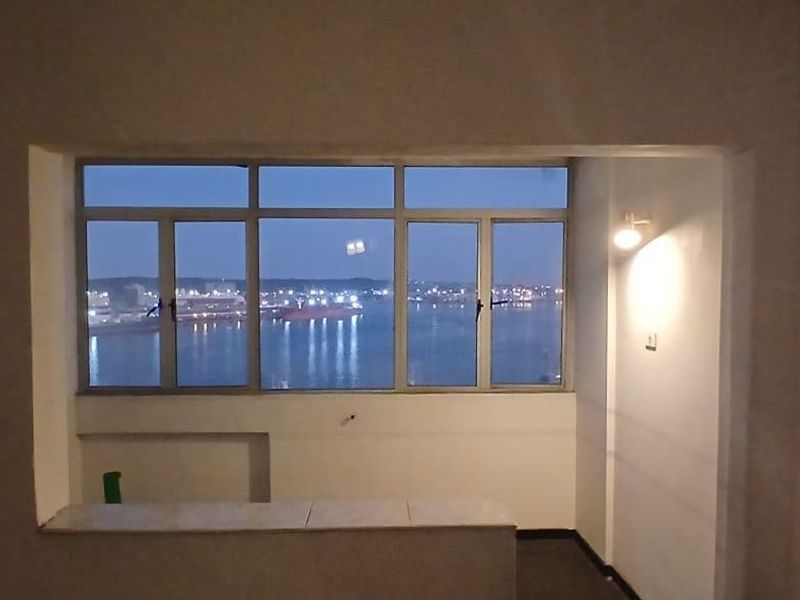 An empty living area featuring a large window with a scenic harbor view and a built-in ledge, offering a bright and open space.