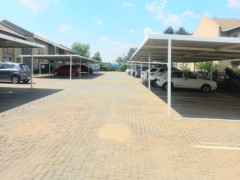 Outdoor parking area featuring multiple covered parking bays with metal structures and paved ground surface.