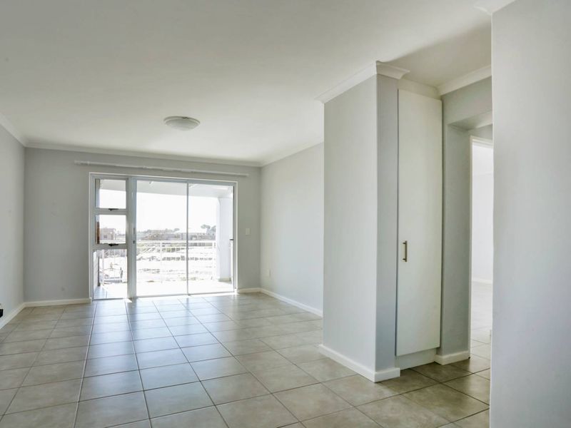 A bright, empty living area featuring neutral tiled flooring, a built-in storage cupboard, and a sliding glass door leading to an outdoor balcony.