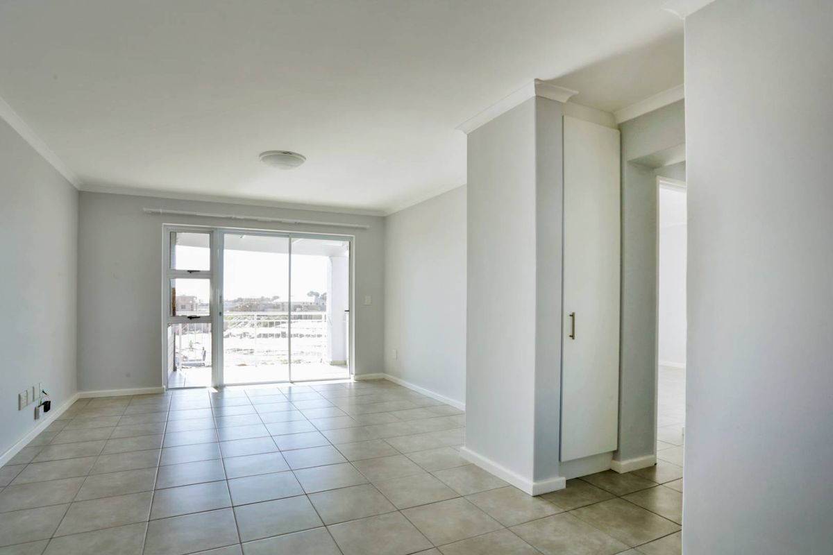 A bright, empty living area featuring neutral tiled flooring, a built-in storage cupboard, and a sliding glass door leading to an outdoor balcony.