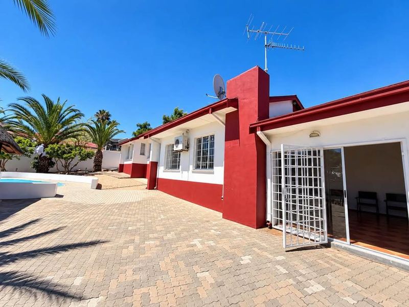 Rear exterior view featuring a paved patio area, swimming pool, and access to the home via a sliding glass door with security gate.