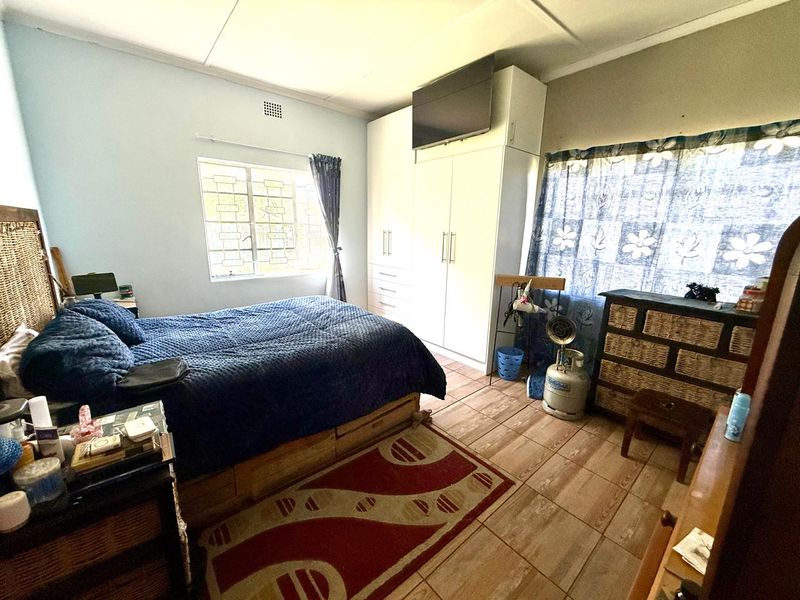 A functional bedroom featuring built-in cupboards, tiled flooring, and security burglar bars on the window.