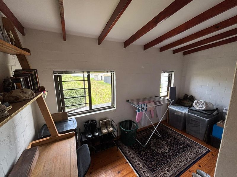 A bedroom featuring exposed timber ceiling beams, painted brick walls, and timber flooring, with natural light provided by steel-framed windows.
