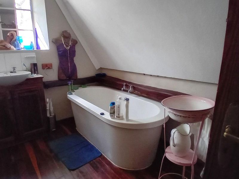 A bathroom featuring a freestanding bathtub, vanity basin, and timber flooring under a sloped ceiling, showing signs of wear and dated finishes.