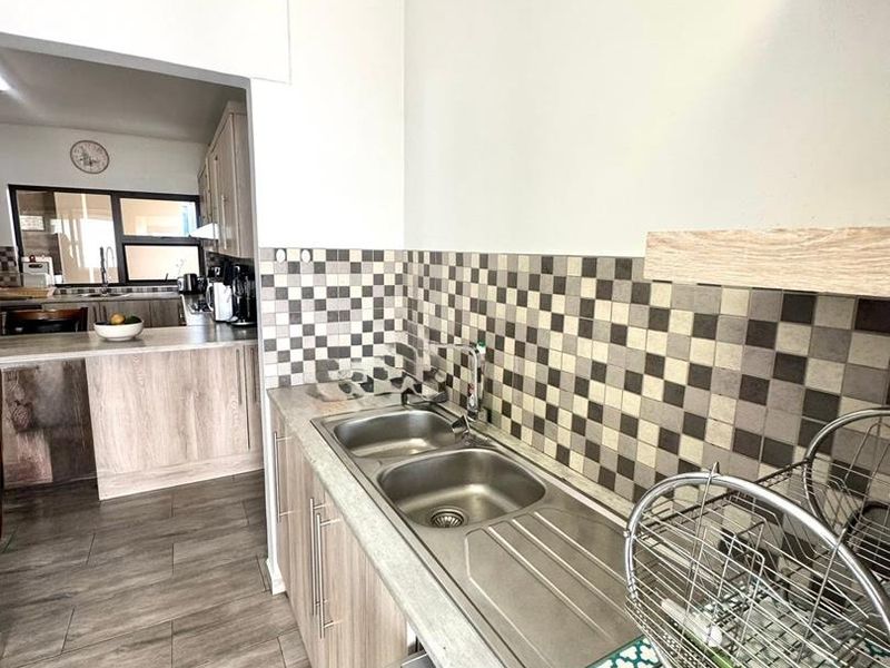 A functional scullery area featuring double stainless steel sinks, modern laminate cabinetry, and a decorative tiled backsplash, providing additional prep and wash-up space.