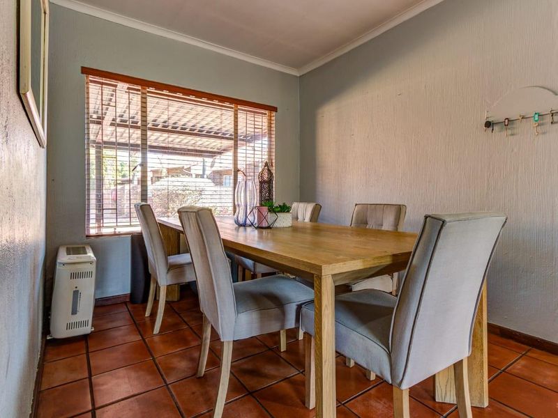A dining room featuring terracotta floor tiles, neutral walls, and a window with venetian blinds, providing a functional space for family meals.