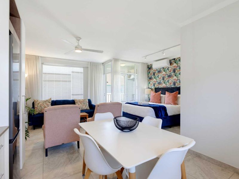 An open-plan living and bedroom area featuring tiled floors, a ceiling fan, track lighting, and a split-system air conditioner with access to a balcony.