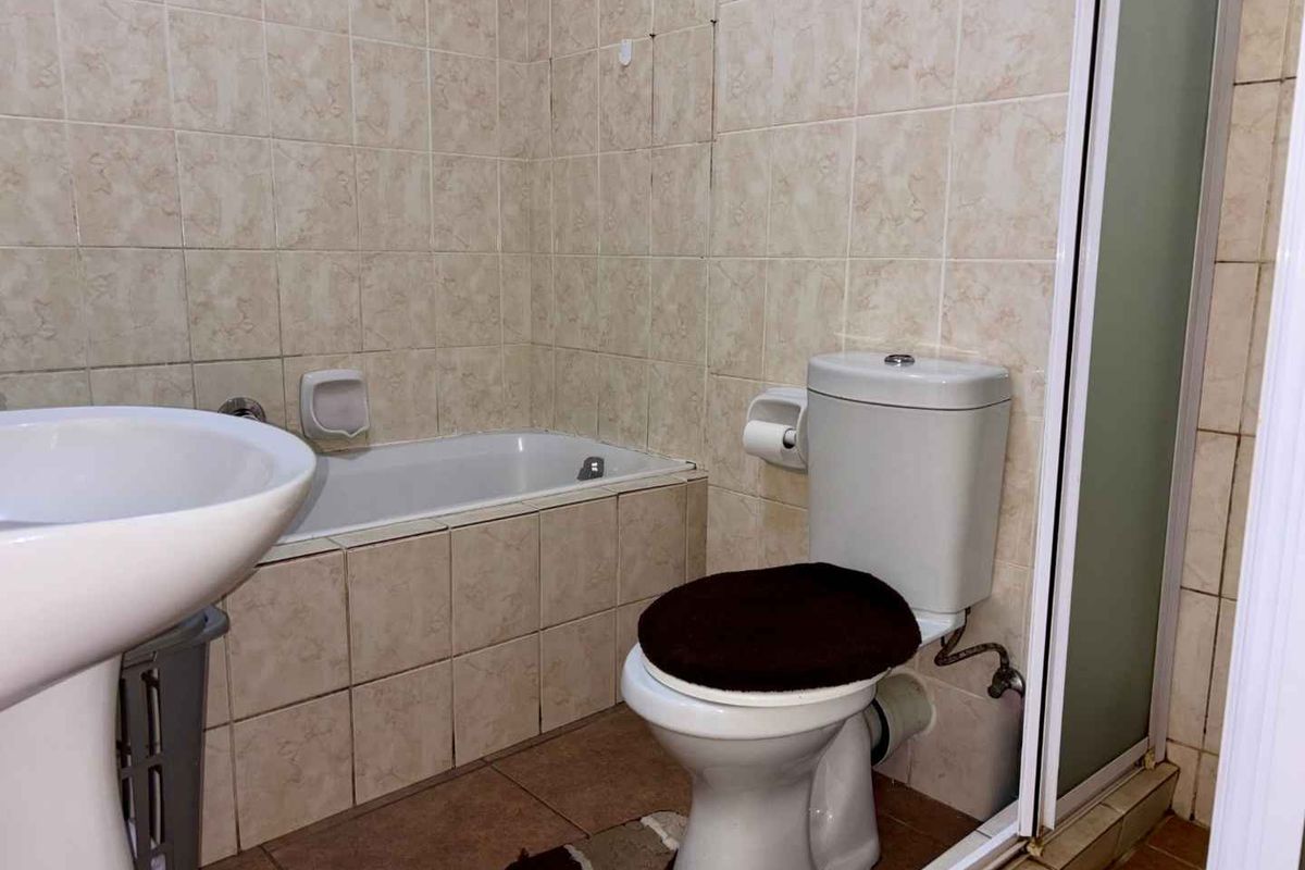 A functional bathroom featuring a built-in bathtub, pedestal sink, and toilet, finished with neutral wall tiling and floor tiles.