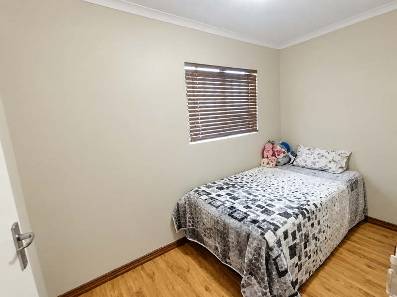 A clean and well-maintained bedroom featuring light-toned walls, laminate flooring, and a window fitted with venetian blinds.