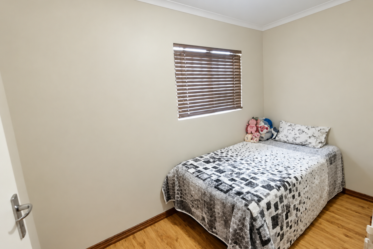 A clean and well-maintained bedroom featuring light-toned walls, laminate flooring, and a window fitted with venetian blinds.