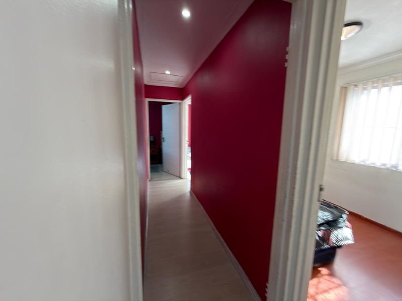 A bright hallway featuring bold red accent walls, light-toned flooring, and recessed ceiling lighting, providing access to adjacent rooms.