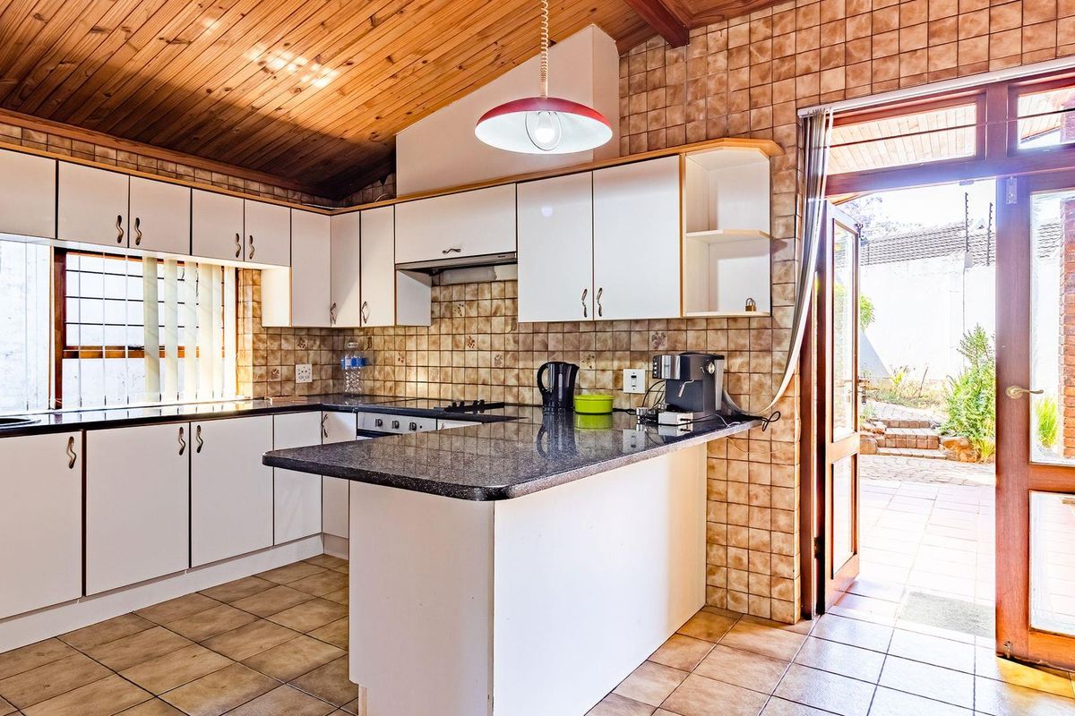 A functional kitchen featuring white cabinetry, granite-look countertops, tiled splashbacks, and a timber-paneled ceiling, with direct access to an outdoor patio area.