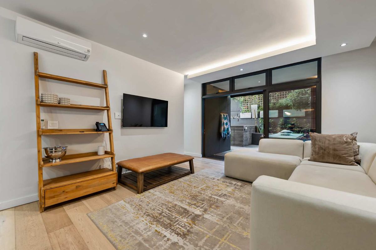 Modern living room featuring timber flooring, recessed cove lighting, and a split-system air conditioner, with direct access to an outdoor patio area.