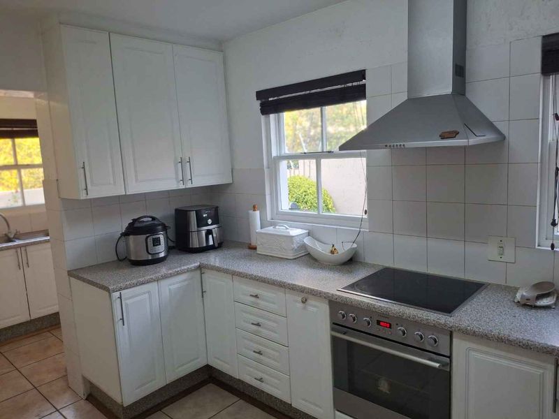 A functional kitchen featuring white cabinetry, granite countertops, a built-in oven with an electric hob, and a stainless steel extractor fan.