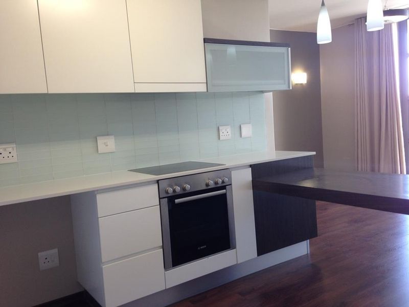 Modern kitchen featuring sleek white cabinetry, stone countertops, a built-in oven, electric cooktop, and a functional breakfast bar extension.