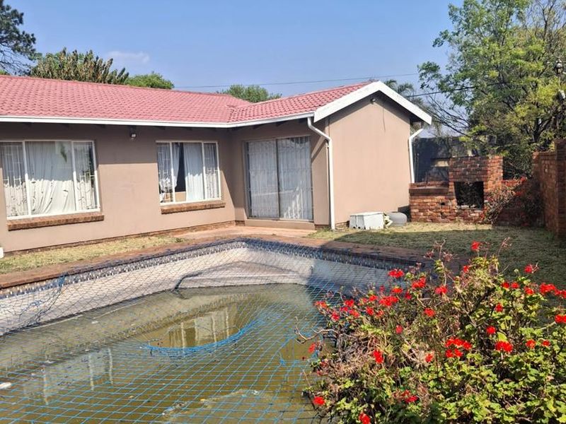 Rear garden area featuring a swimming pool with safety net, brick built-in braai, and paved surrounds adjacent to the main house structure.