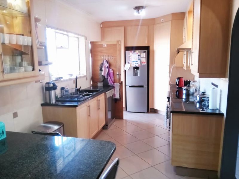 A functional kitchen featuring light wood cabinetry, dark granite countertops, ceramic floor tiles, and integrated appliances, offering a practical layout for daily use.
