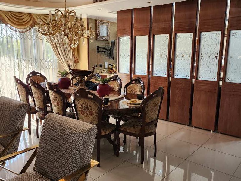 Formal dining area featuring polished tiled flooring, a decorative recessed ceiling, and integrated wood paneling with glass inserts.