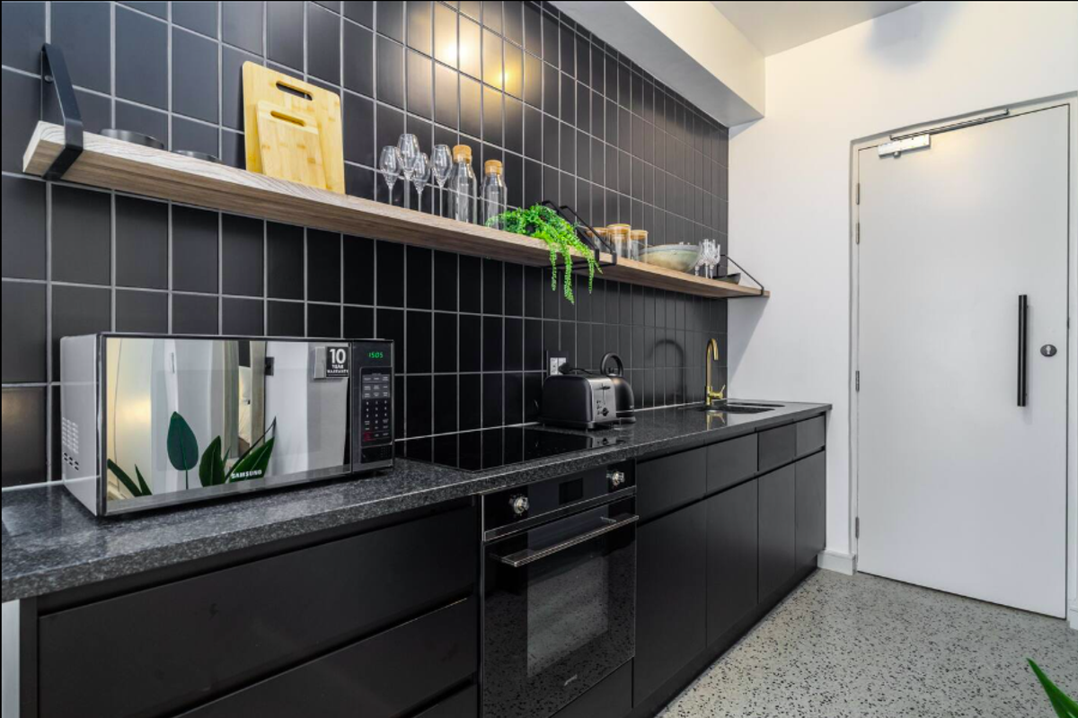Modern kitchen featuring sleek black cabinetry, dark granite countertops, integrated oven, induction hob, and stylish black tiled splashback with floating timber shelving.