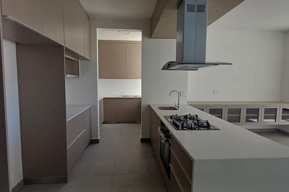 Modern kitchen featuring sleek cabinetry, stone countertops, a central island with a gas hob, and a separate scullery area with additional storage.