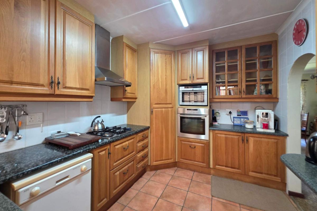 A functional kitchen featuring traditional timber cabinetry, granite-look countertops, built-in oven, microwave, and gas cooktop with stainless steel extractor fan.