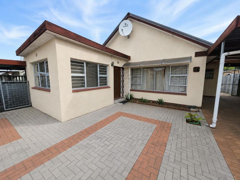 Front elevation of a residential house featuring a paved driveway, aluminium window frames, and a secure entrance with a security gate.